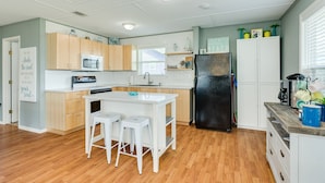 A modern kitchen with wooden cabinets, a white countertop, a black refrigerator, and a small island with stools. - Dream | Steps to the Beach | Large Deck (Crystal Beach)