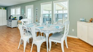 A dining area with a round table set for four, surrounded by white chairs. There is a kitchen area with white cabinets and a coffee maker visible in the background. - Dream | Steps to the Beach | Large Deck (Crystal Beach)