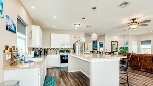 A modern kitchen with white cabinets, a central island, and a dining area with a brown leather couch.