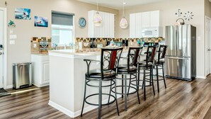 A modern kitchen with white cabinets, a stainless steel refrigerator, and a bar area with stools.
