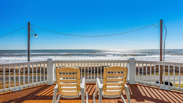 A wooden deck with two rocking chairs facing the ocean.