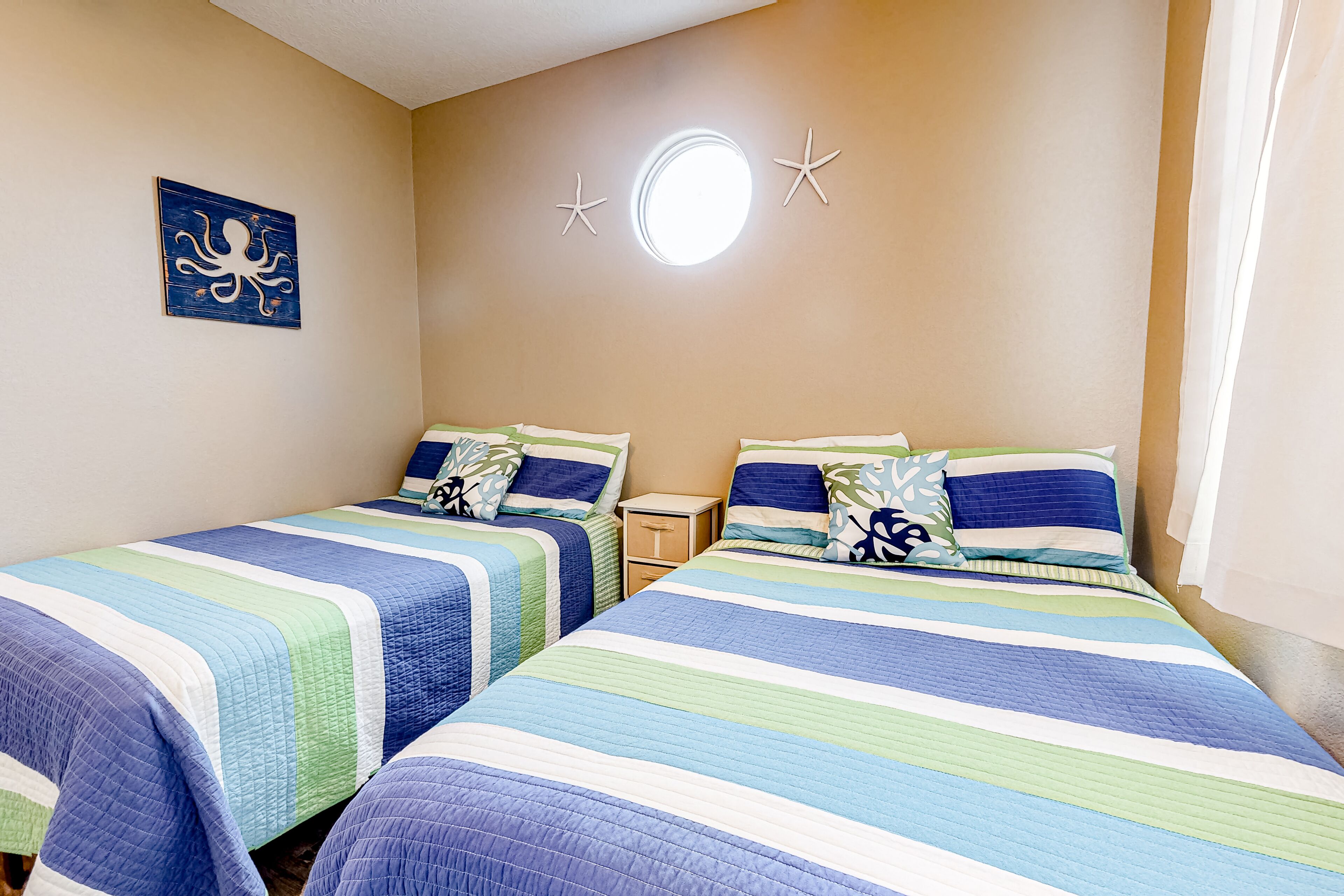 A room with two beds, each with striped bedding, a small bedside table, and a wall decoration.