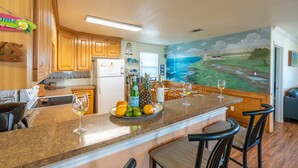 Una cocina con armarios de madera, encimera de granito y un mural con un paisaje costero.