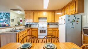 Una cocina con armarios de madera, una estufa blanca y un refrigerador. Hay una mesa de comedor con platos y sillas.