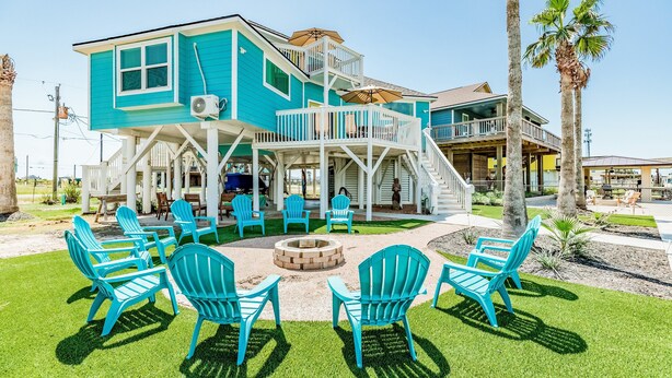 A turquoise two-story house with a deck, outdoor seating, and a fire pit. - Dream | Canal Front | Firepit | Kayking & Fishing (Surfside Beach)
