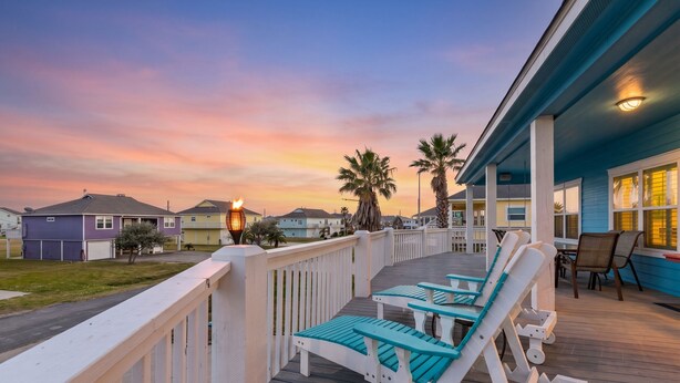 A wooden deck with lounge chairs, a railing, and a view of houses and palm trees. - Perfect | Steps to Beach | Firepit | Sleeps 10 (Crystal Beach)