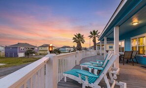 Um deck de madeira com espreguiçadeiras, guarda-corpo e vista para casas e palmeiras.