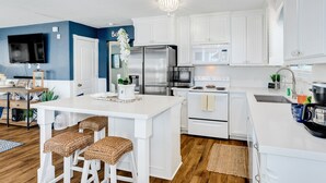 A modern kitchen with white cabinetry, stainless steel appliances, and a central island with bar stools.