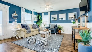 A living room with a blue wall, a ceiling fan, a TV, a sofa, a coffee table, and a patterned rug.