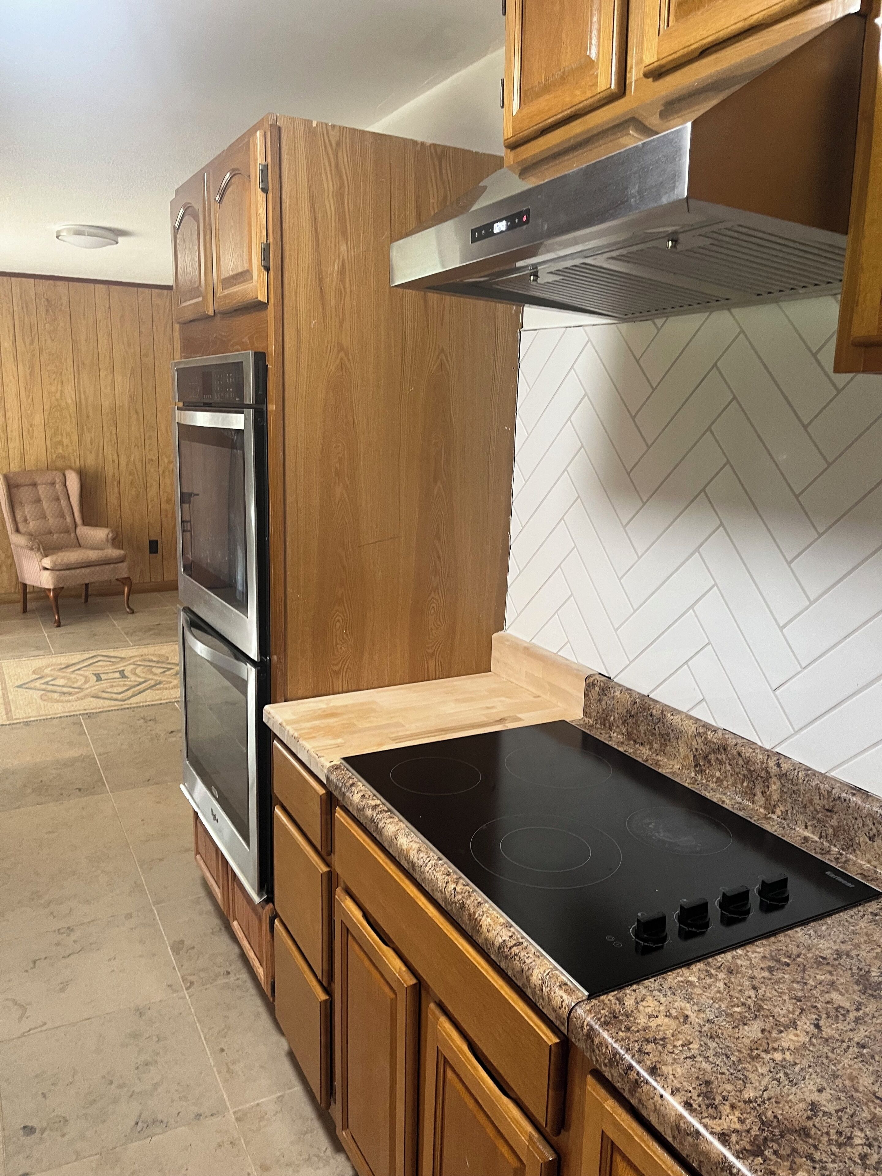 Une cuisine avec des armoires en bois, une hotte de cuisine en acier inoxydable, une plaque de cuisson noire et un dosseret décoré d’un motif en chevrons.