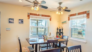 A dining area with a table set for four, two ceiling fans, and large windows with a view. - Retreat | Gulf Views | Large Deck | Family Fun (Surfside Beach)