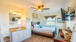 A bedroom with a bed, a ceiling fan, a TV mounted on the wall, and a window with curtains. - Retreat | Gulf Views | Large Deck | Family Fun (Surfside Beach)