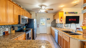 A kitchen with wooden cabinets, granite countertops, a microwave, stove, and a ceiling fan. - Retreat | Gulf Views | Large Deck | Family Fun (Surfside Beach)
