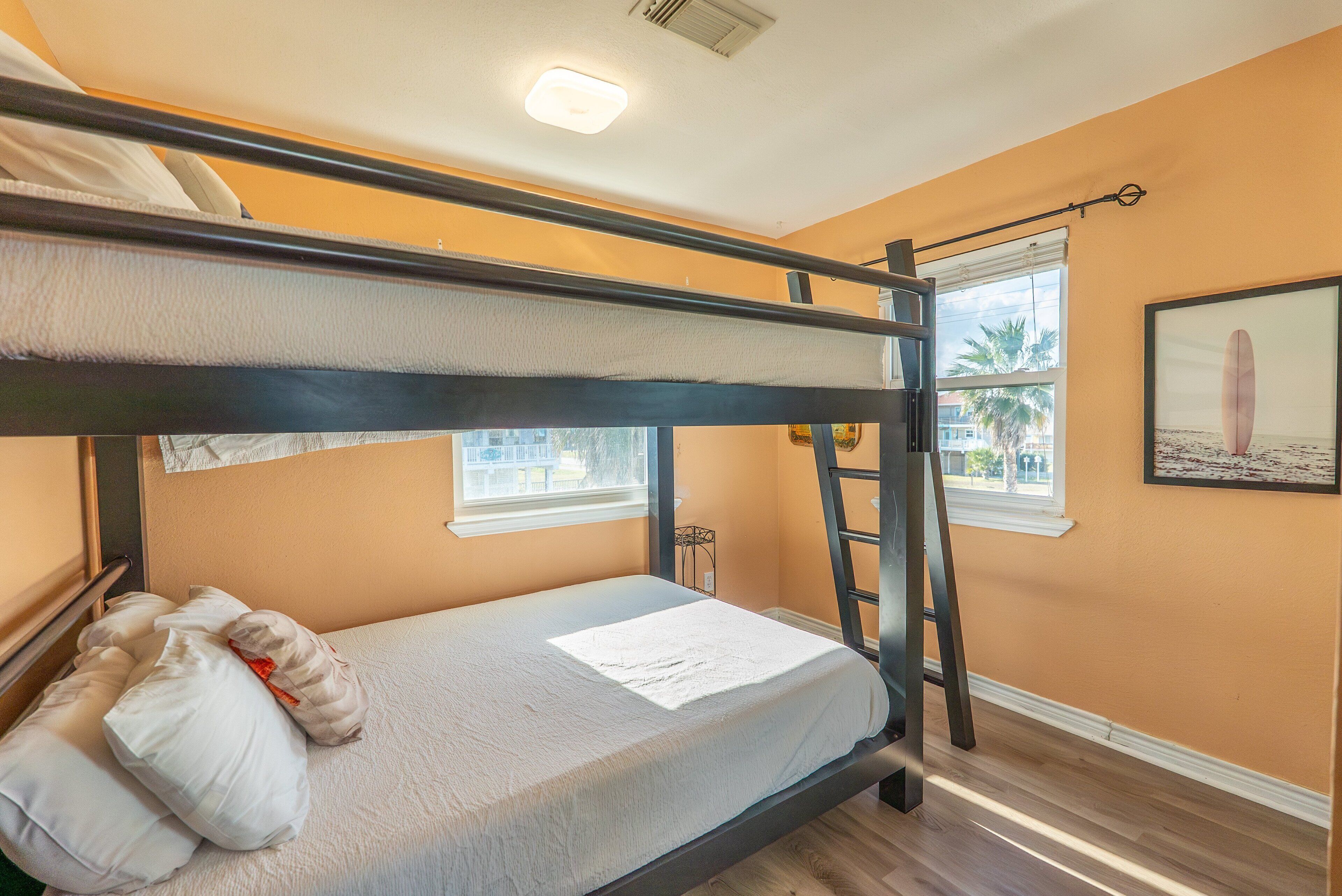 A bunk bed with a white mattress and pillows, a ladder, and a window with a view of palm trees.