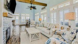 A spacious living room with a fireplace, a ceiling fan, and a large window with the word "OCEAN" on the wall.