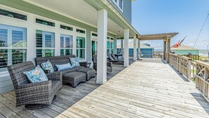 A covered outdoor deck with wicker furniture and a view of the ocean.
