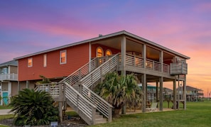 A two-story house with a balcony, a staircase, and a covered porch area. - Steps to the Beach | Tropical Theme | Pet Paradise (Crystal Beach)