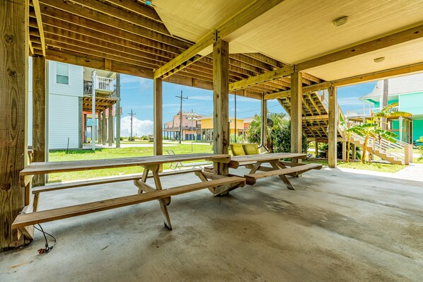 An outdoor covered area with picnic tables and a view of buildings in the background.