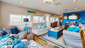 A spacious living room with a large window, a television, and a sign that reads "Relax at the Beach." - Haven | Ocean View | Large Deck | Pet Friendly (Surfside Beach)