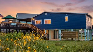 A two-story building with a blue exterior, a wooden deck with a railing, and a sign that reads 'Blue Skies.' - Haven | Ocean View | Large Deck | Pet Friendly (Surfside Beach)