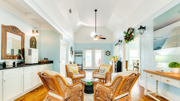 A spacious living room with wicker furniture, a ceiling fan, and a large mirror. - Perfect | Gulf Views | Furnitured Deck | Sleeps 10 (Gilchrist)