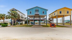 A beachfront property with a central blue house, two side structures, and a covered area with a vehicle. - Perfect | Gulf Views | Furnitured Deck | Sleeps 10 (Gilchrist)
