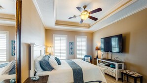A bedroom with a bed, bedside tables, a dresser, a TV, and a ceiling fan.