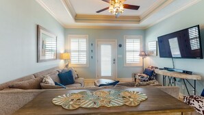 A living room with a wooden coffee table, a ceiling fan, and a television mounted on the wall.