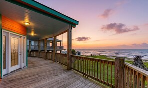 A wooden deck with a railing, a covered porch, and a view of the ocean at sunset. - Beachfront l Free Cancellation l Fenced Yard (Gilchrist)