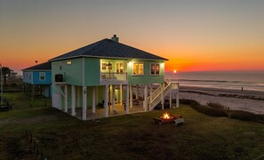 Une maison avec un balcon, un foyer extérieur et une vue sur le coucher de soleil sur l’océan.