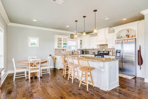 A kitchen with white cabinets, a central island with bar stools, a stainless steel refrigerator, and wooden flooring.