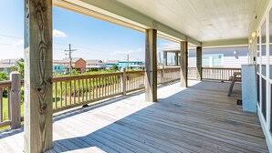Eine Holzterrasse mit Geländer, einem überdachten Bereich und Blick auf Häuser und Grünflächen im Hintergrund.