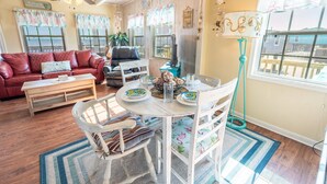 A cozy living room with a red leather couch, a wooden coffee table, a dining table with chairs, and a view of the outdoors through large windows. - Prime | Beachfront | Beach Access | Sleeps 8 (Surfside Beach)
