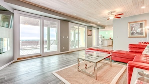 A spacious living room with a red sofa, a glass coffee table, and a large sliding glass door leading to a balcony. - Beachfront 4br, Hot Tub, Multiple Deck, Sleeps 16 (Gilchrist)