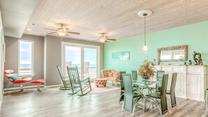 A spacious room with a dining area, two rocking chairs, a glass table, and a view of the ocean through large windows. - Beachfront 4br, Hot Tub, Multiple Deck, Sleeps 16 (Gilchrist)