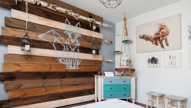 A bedroom with a wooden headboard, a bed with white bedding, a nightstand with a lamp, and a wall with framed artwork. - Wild and Free Urban Jungle Apartment (Łódź)