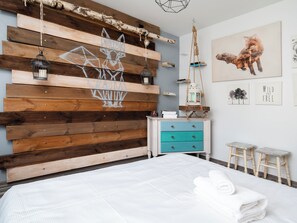 Un dormitorio con cabecera de madera, cama con ropa de cama blanca, mesita de noche con lámpara y una pared decorada con cuadros.