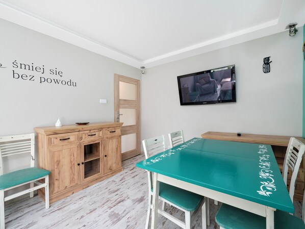 Una habitación con un armario de madera, una mesita de noche color turquesa con diseños florales blancos y un televisor montado en la pared.