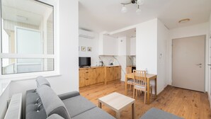 Una sala moderna con un sofá gris, una mesa de comedor de madera y una zona de cocina con armarios de madera y un televisor.