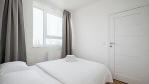 Un dormitorio con cama, ventana con cortinas y puerta.