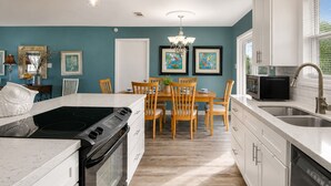 A modern kitchen with a central island, white cabinetry, and a dining area with wooden chairs.