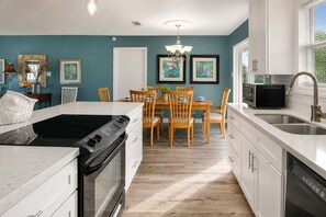 A modern kitchen with a central island, white cabinetry, and a dining area with wooden chairs.