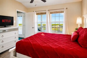 A bedroom with a large bed, a television, a dresser, and a balcony with a view. - Prime | Gulf Views | Large Deck | Pet Paradise (Crystal Beach)