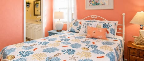 Une chambre à coucher avec un lit, une table de chevet, une lampe, une commode et une fenêtre avec des rideaux.