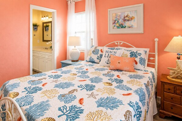 A bedroom with a bed, a nightstand, a lamp, a dresser, and a window with curtains.