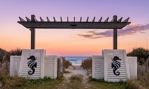 A wooden pergola entrance with a seahorse design, leading to a beach path.