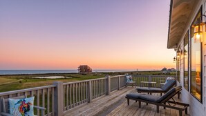 A wooden deck with lounge chairs and a railing overlooking a beach at sunset. - Luxury Ocean View l Pool l Free Cancellation (Crystal Beach)