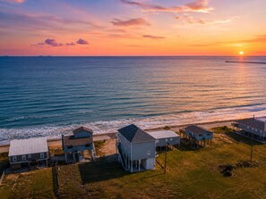 A coastal property with multiple houses, a dock, and a view of the ocean at sunset. - Luxury | Beachfront | Family Fun | Sleeps 22 (Surfside Beach)