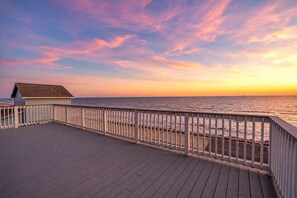 A wooden deck with a railing overlooking a body of water at sunset. - Luxury | Beachfront | Family Fun | Sleeps 22 (Surfside Beach)