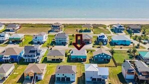 Zona residencial costera con casas dispuestas en filas, una playa al fondo y una flecha roja señalando una casa en particular.